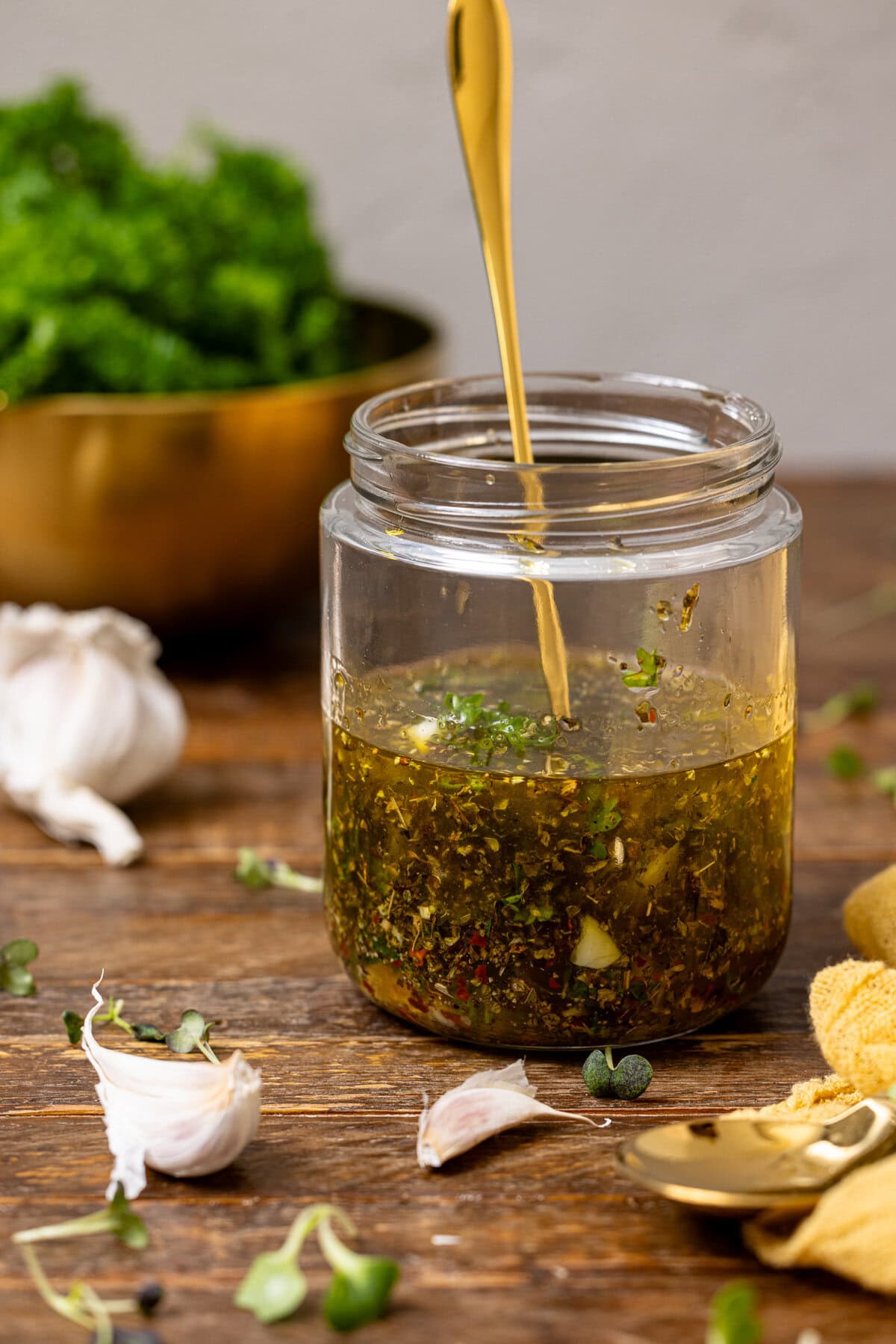 Italian dressing in a mason jar with a gold spoon with herbs and garlic.