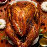 Overhead shot of roasted turkey on a burnt orange table with thanksgiving decor.