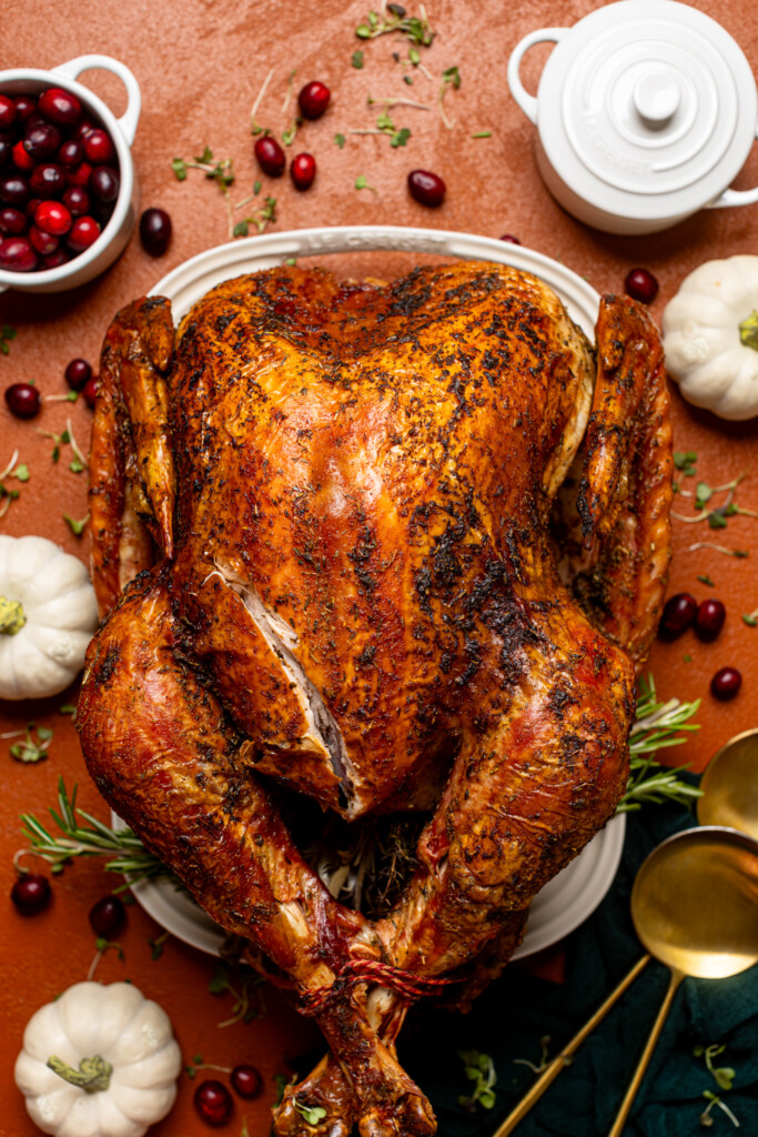 Overhead shot of roasted turkey on a burnt orange table with thanksgiving decor.