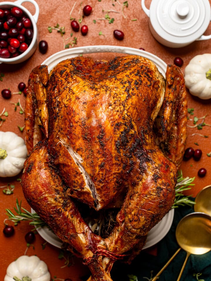 Overhead shot of roasted turkey on a burnt orange table with thanksgiving decor.