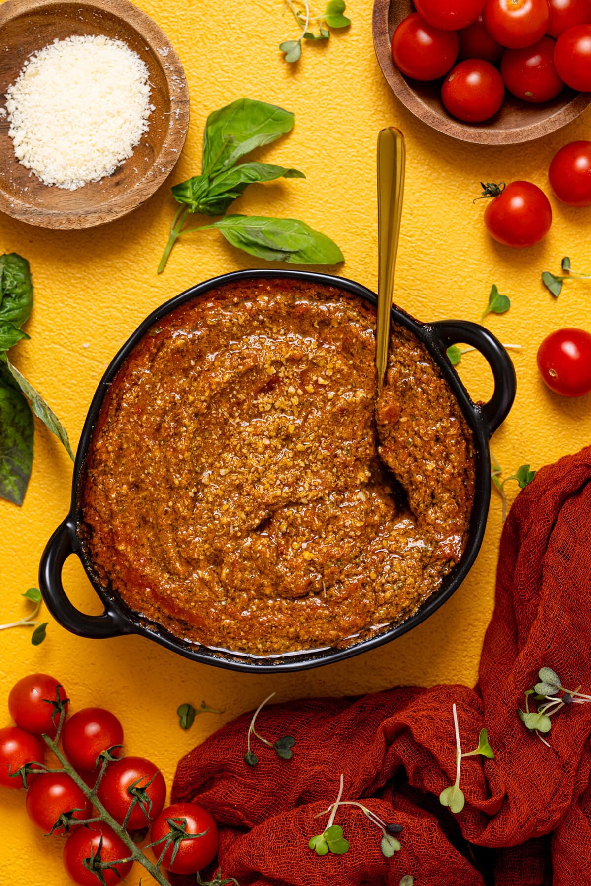 Tomato pesto on a yellow table with tomatoes and basil leaves.