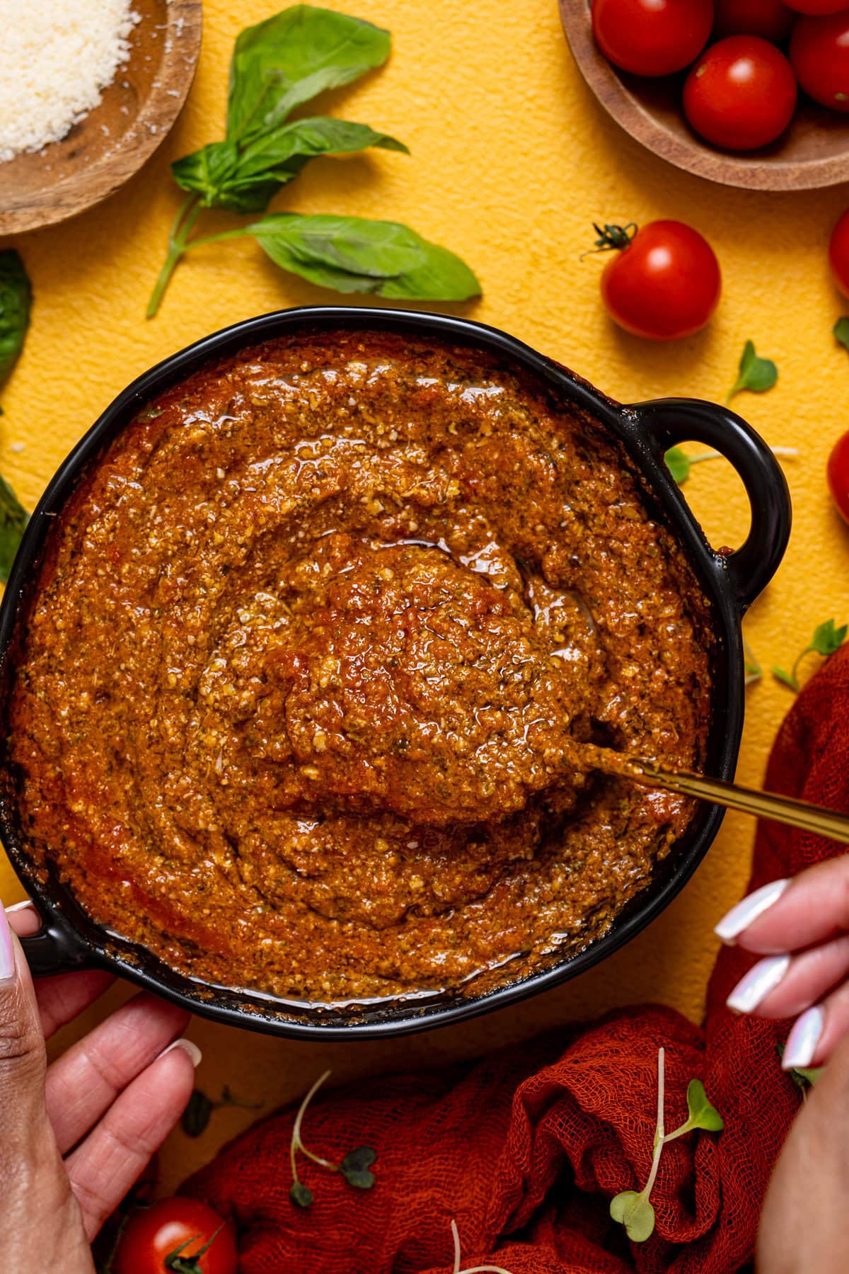 Tomato pesto in a black bowl being held with a spoon.