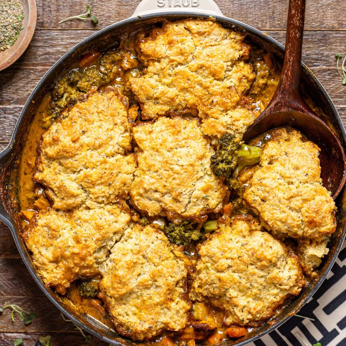 Broccoli cheddar pot pie in a skillet with a wooden spoon on a brown wood table.