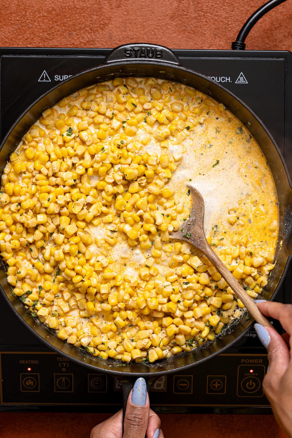 Corn and ingredients in a skillet being cooked + stirred with a spoon.