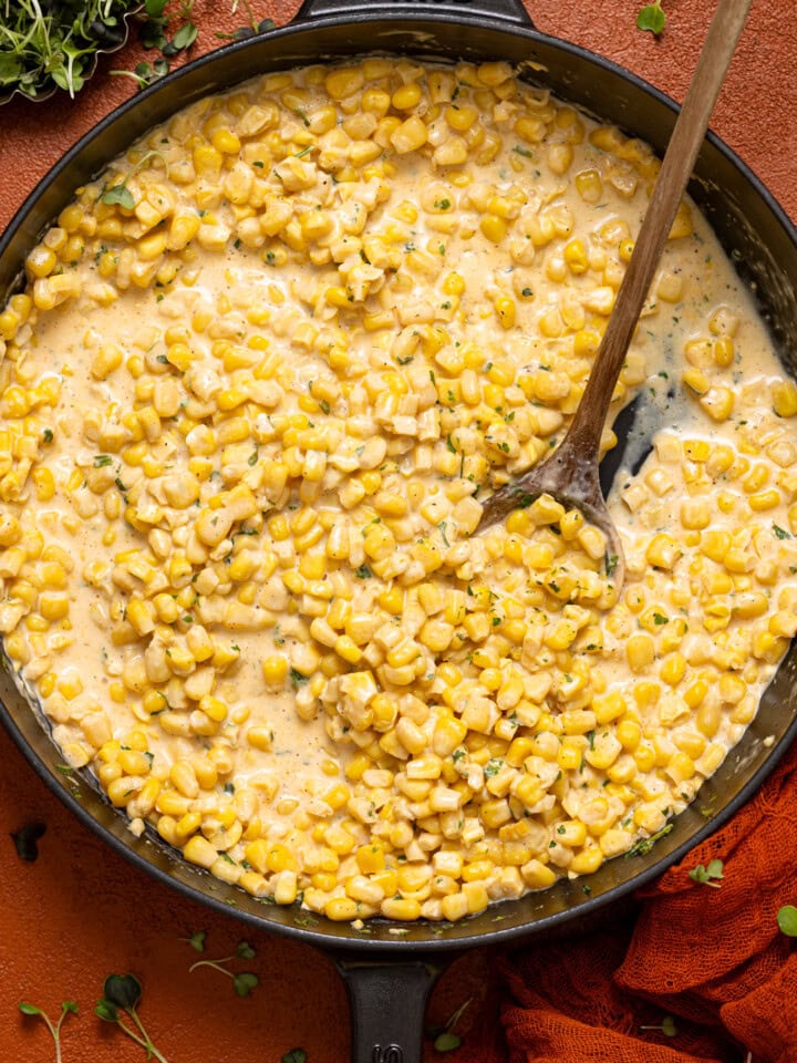 Creamed corn in a black skillet with a wooden spoon.