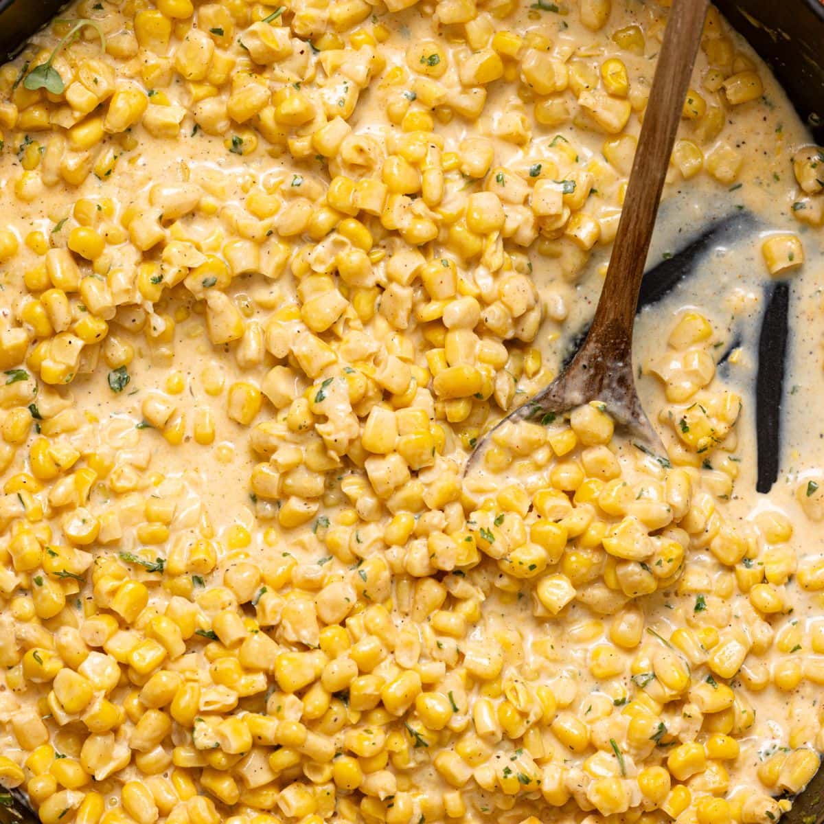 Creamed corn in a black skillet with a wooden spoon.