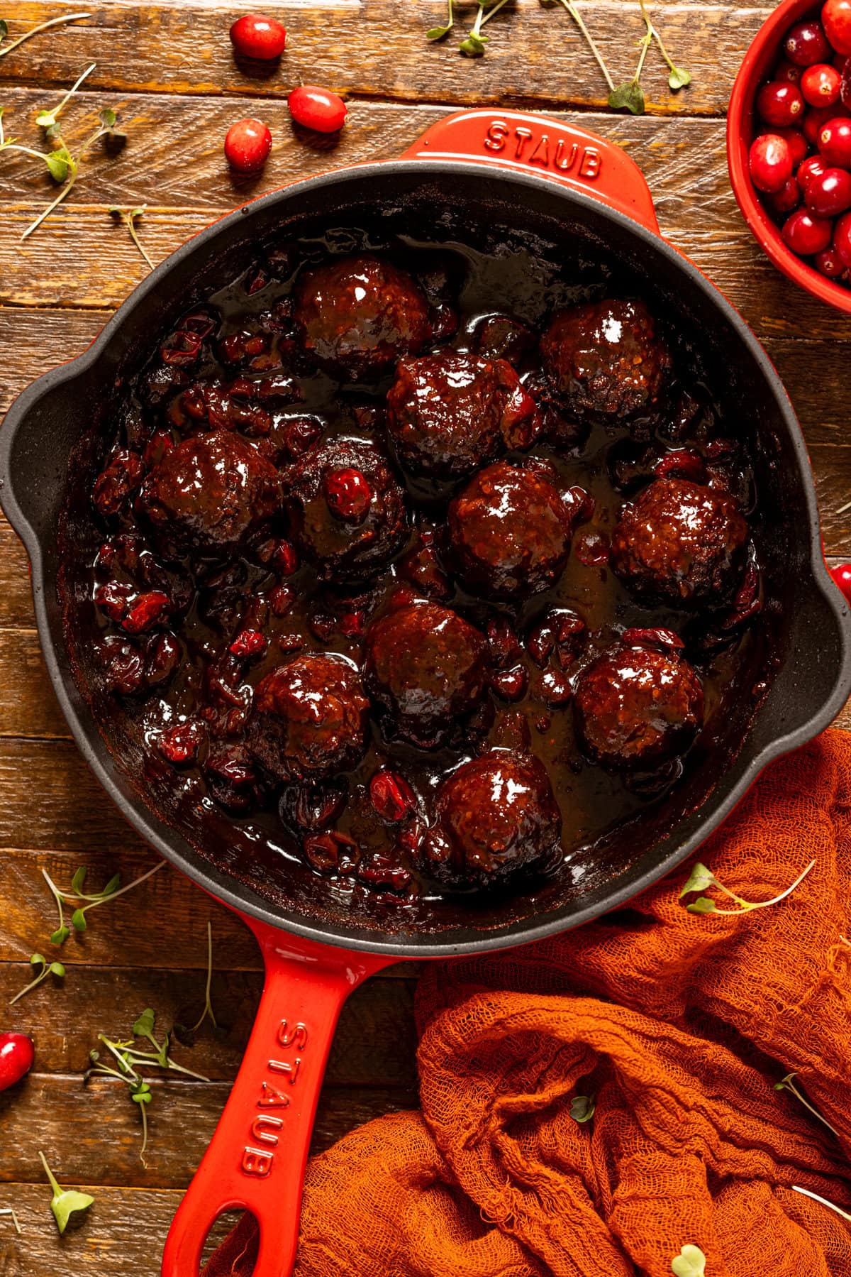 BBQ Jerk meatballs in a red skillet on a brown wood table.