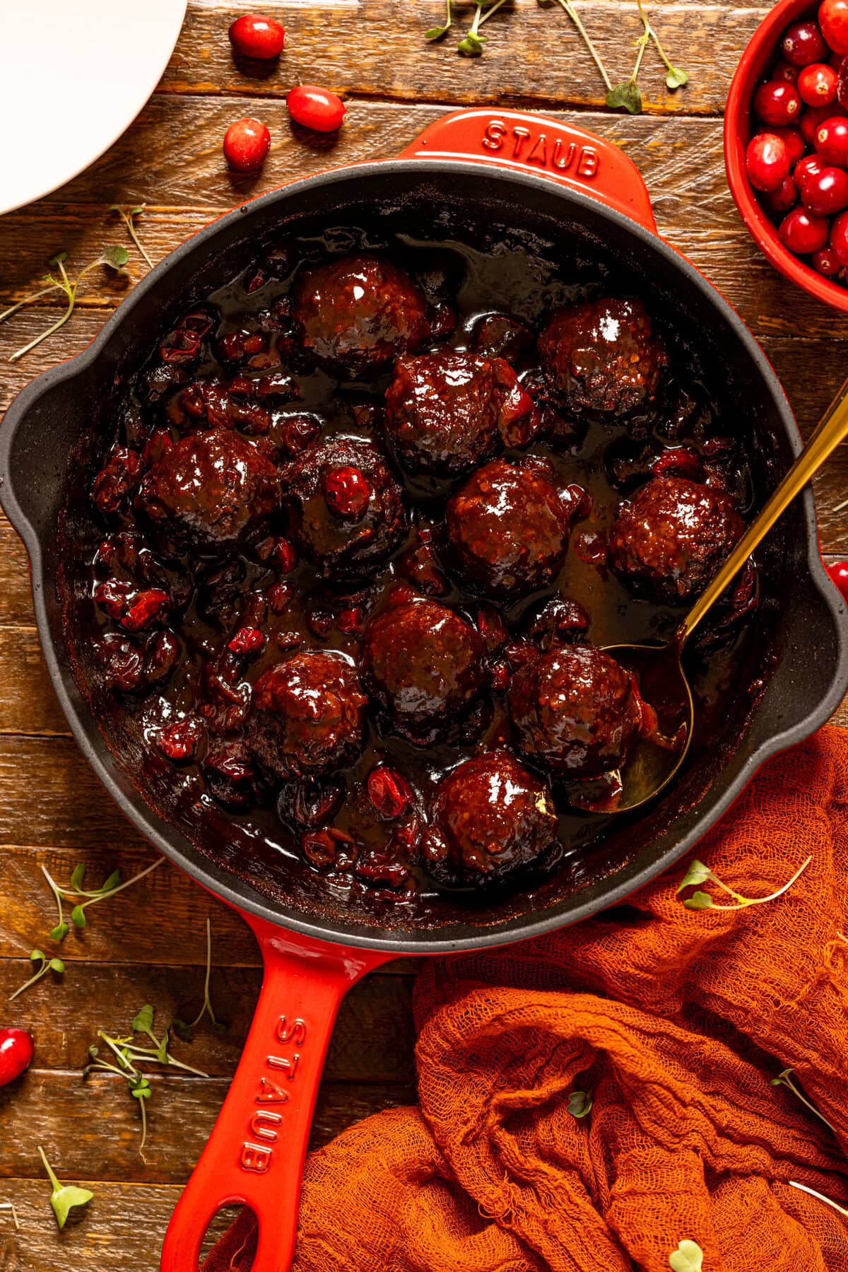 Cranberry BBQ Jerk meatballs in a red skillet with a spoon.