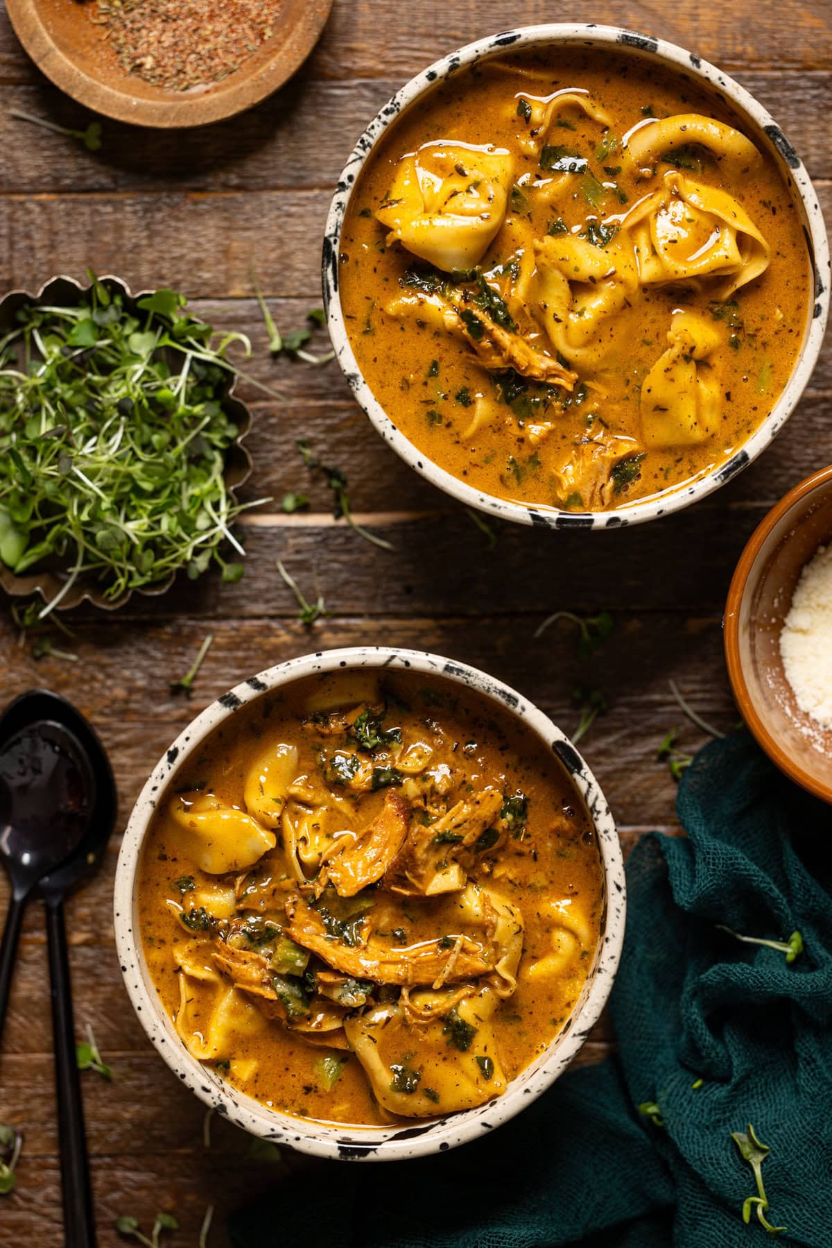 Two bowls of chicken tortellini soup on a brown wood table.