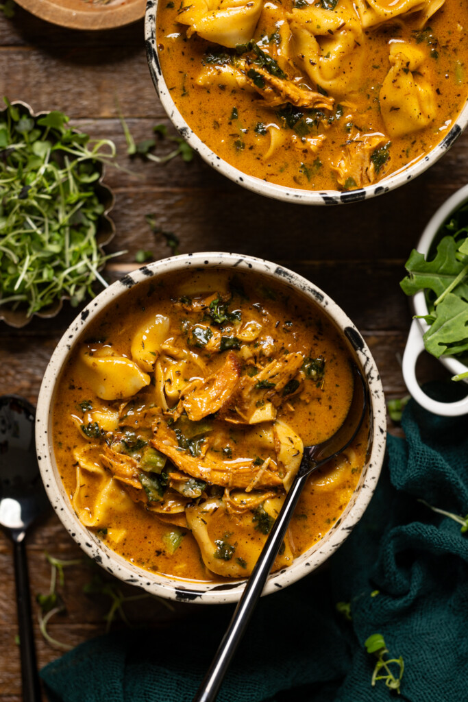 Up close shot of cream blackened chicken tortellini soup with a spoon.