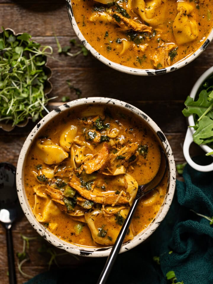 Up close shot of cream blackened chicken tortellini soup with a spoon.