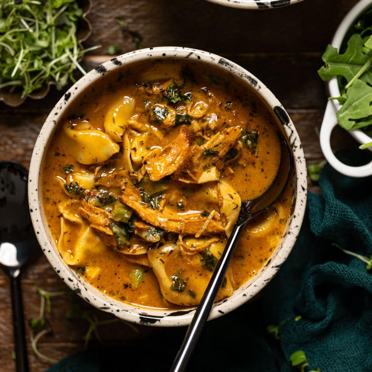 Up close shot of cream blackened chicken tortellini soup with a spoon.