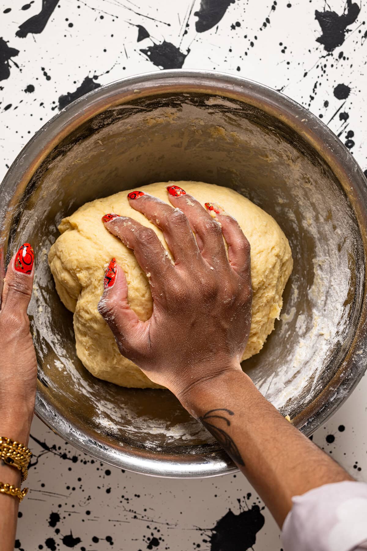 A bowl with the dough being kneaded with hands.