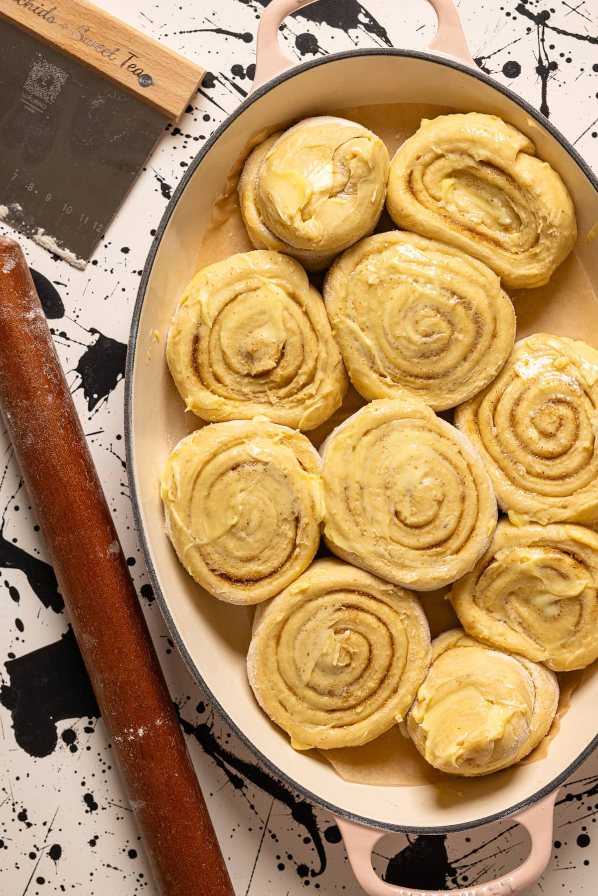 Cinnamon rolls in a baking dish with a rolling pin and dough scraper.