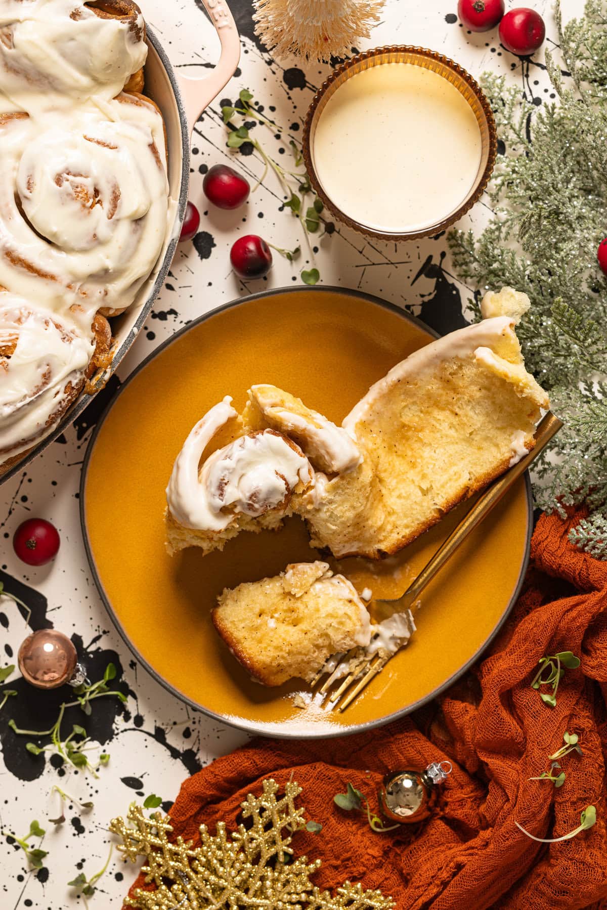 Eggnog cinnamon roll on a yellow plate opened with a form and a glass of eggnog.