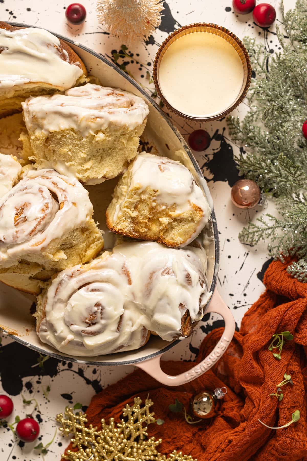 Eggnog cinnamon rolls in a baking dish with a glass of eggnog with Christmas decor.