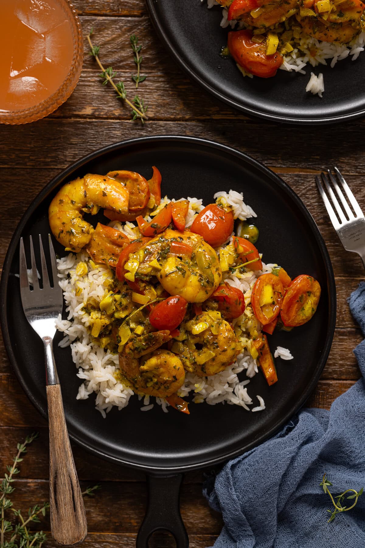 Curry shrimp and white rice on a black plate with forks and a drink.