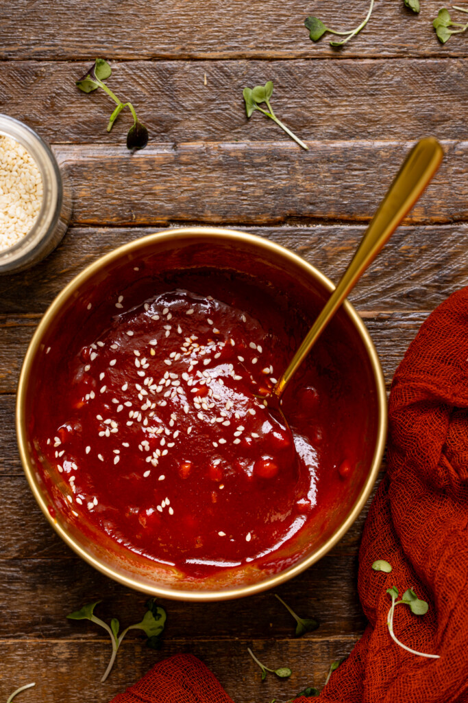 Gochujang sauce in a gold bowl with a spoon on a brown wood table.