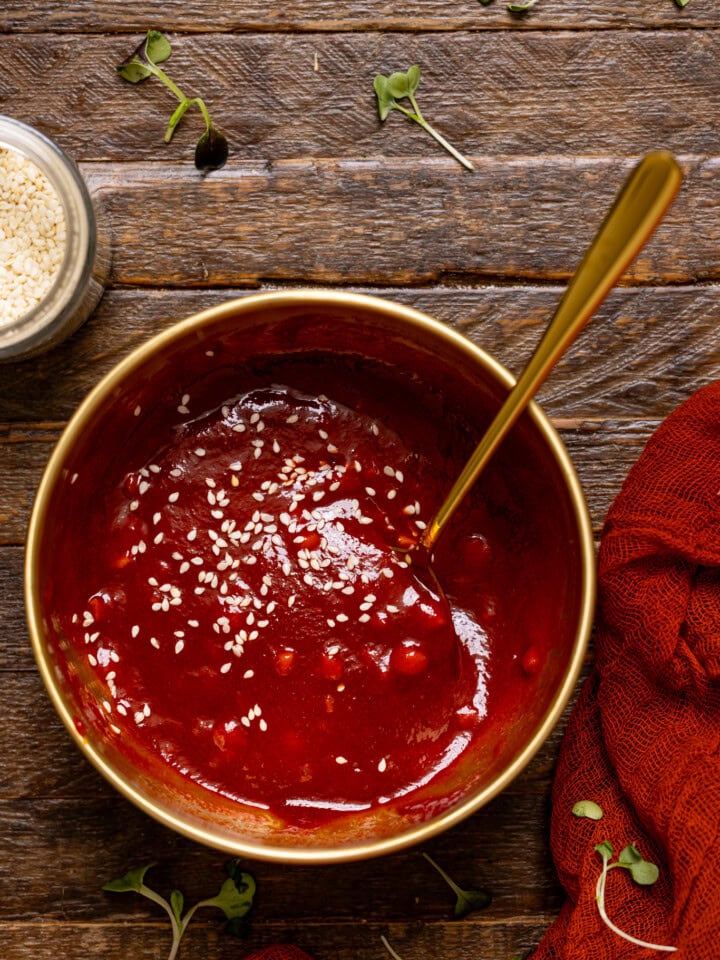 Gochujang sauce in a gold bowl with a spoon on a brown wood table.