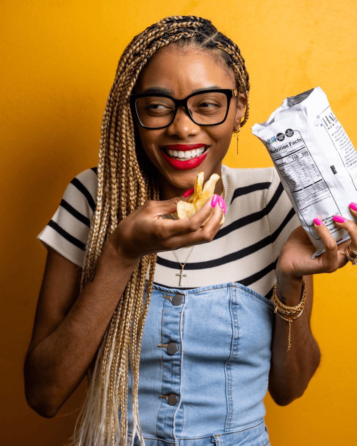 Shanika smiling while holding a bag of chips with a yellow background.