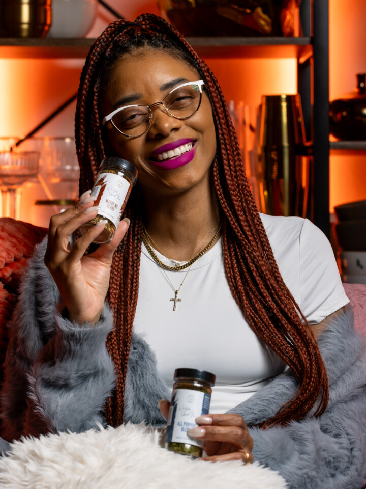 Image of Shanika sitting on a couch smiling while holding seasoning blends.