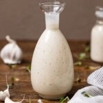 Bottles of creamy Caesar dressing on a wood table with garlic cloves.