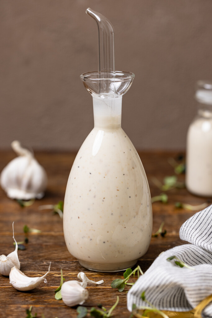 Bottles of creamy Caesar dressing on a wood table with garlic cloves.