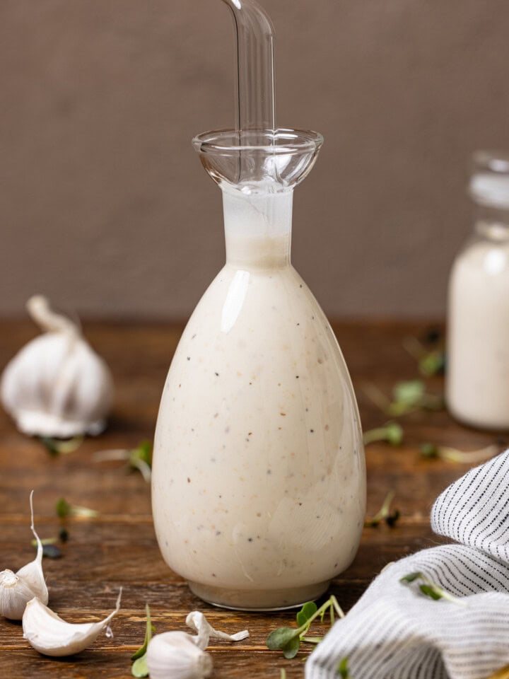 Bottles of creamy Caesar dressing on a wood table with garlic cloves.