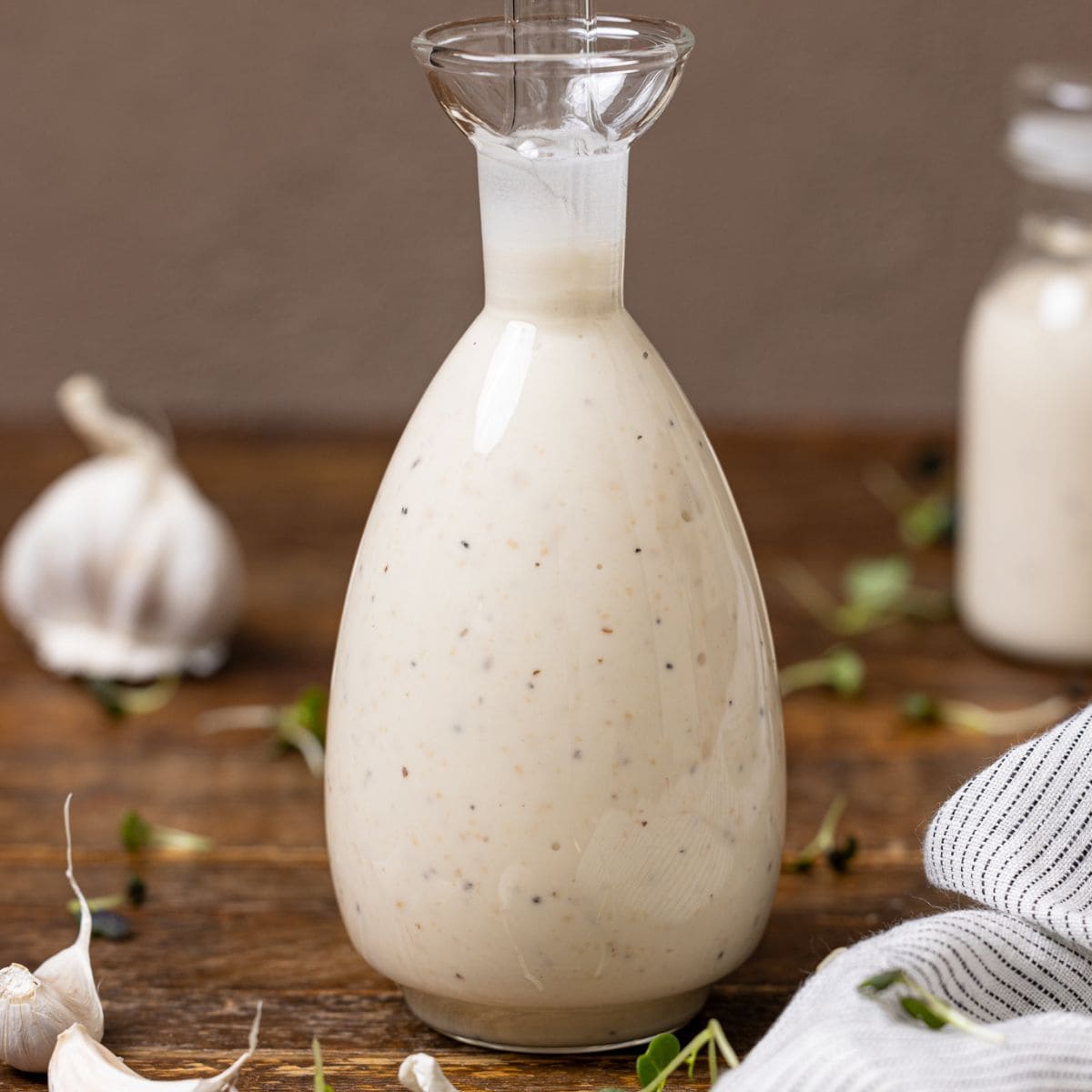 Bottles of creamy Caesar dressing on a wood table with garlic cloves.