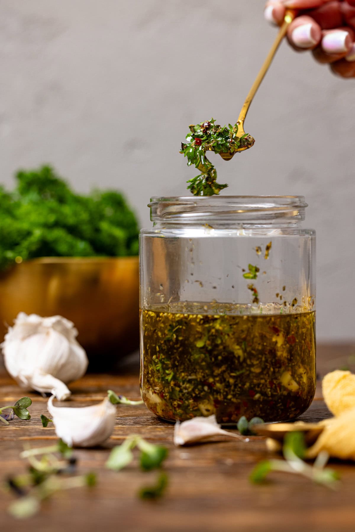 Italian dressing in a mason jar being held up with a spoon with garlic.