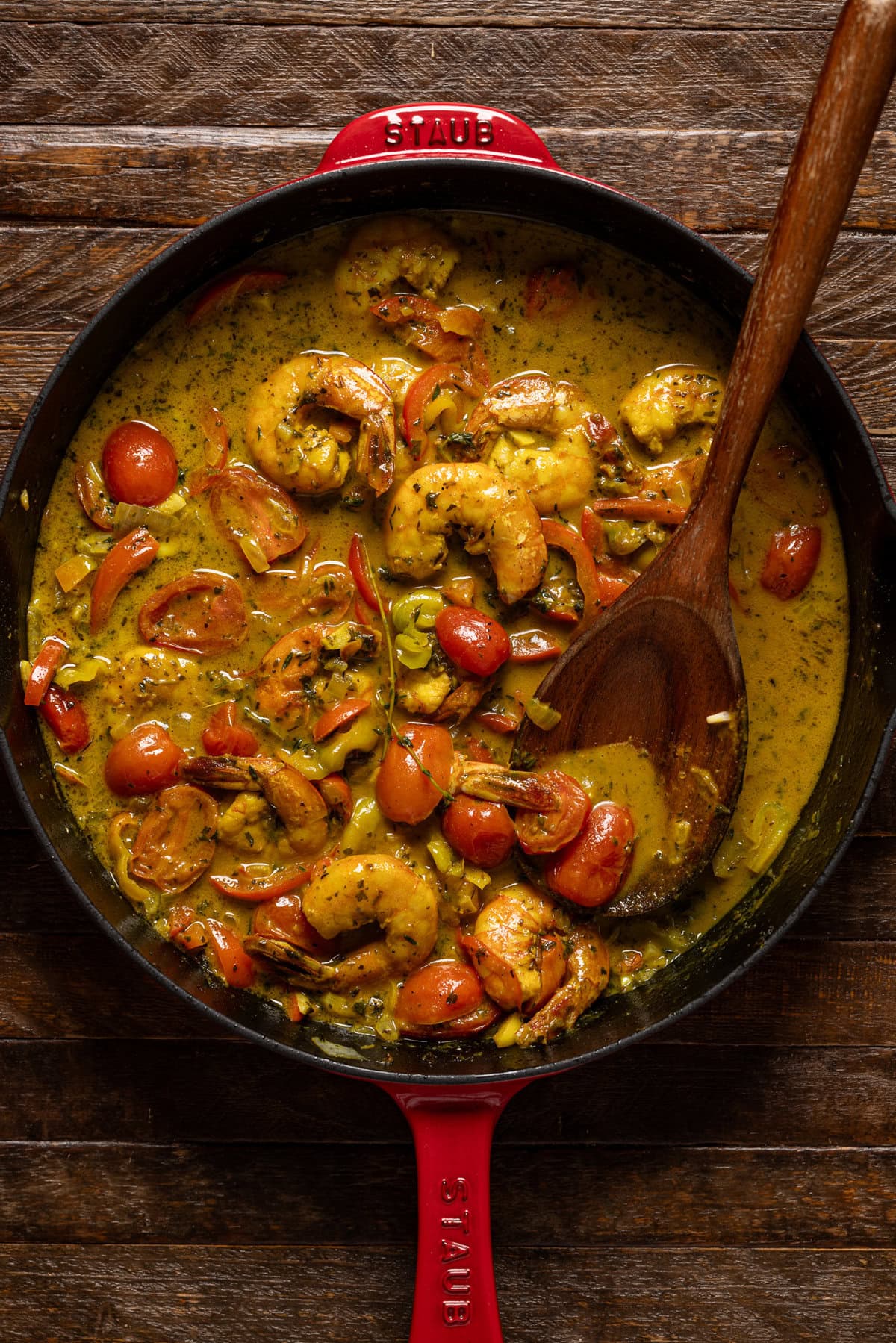 Curry shrimp in a red skillet with a wooden spoon.