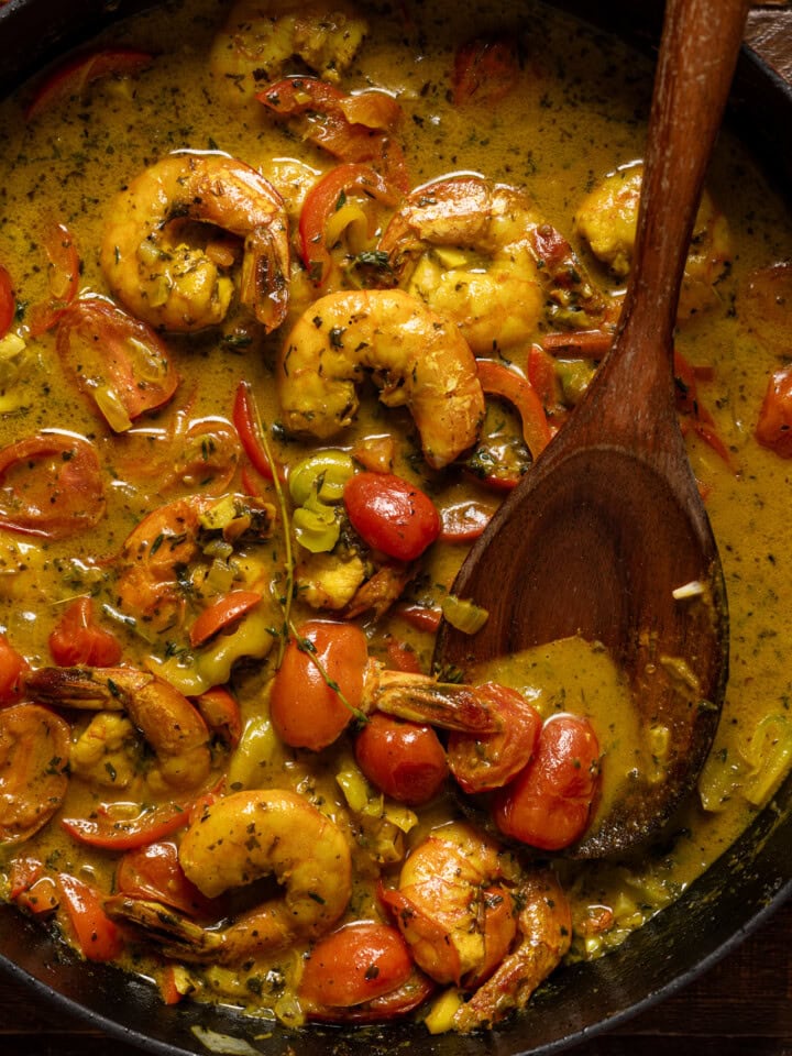 Up close shot of curry shrimp with a wooden spoon.