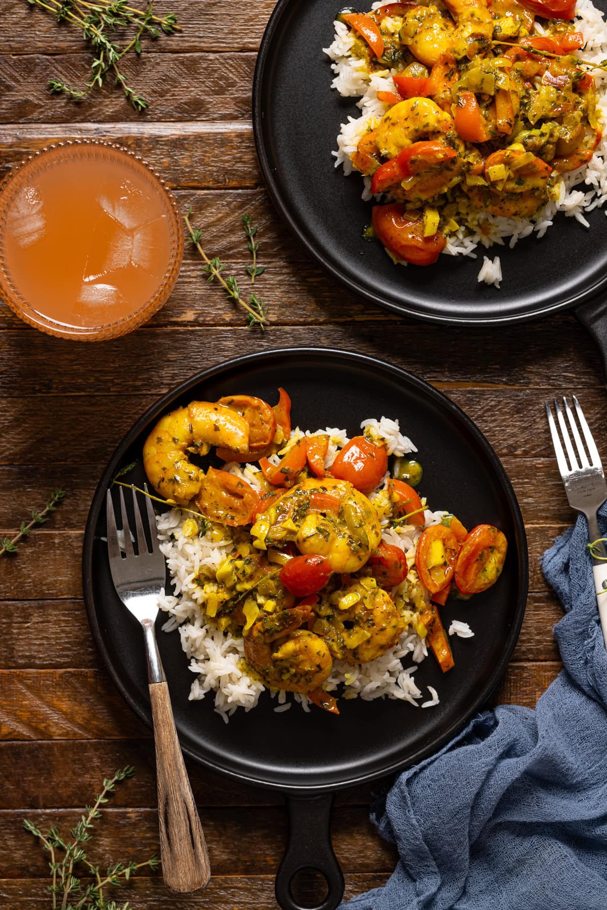 Curry shrimp on black plates with forks and a drink.