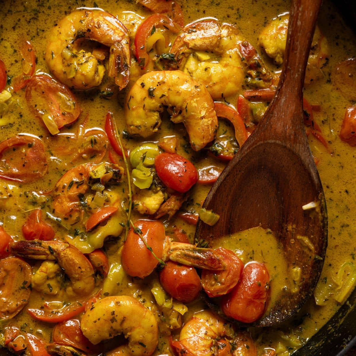 Up close shot of curry shrimp with a wooden spoon.