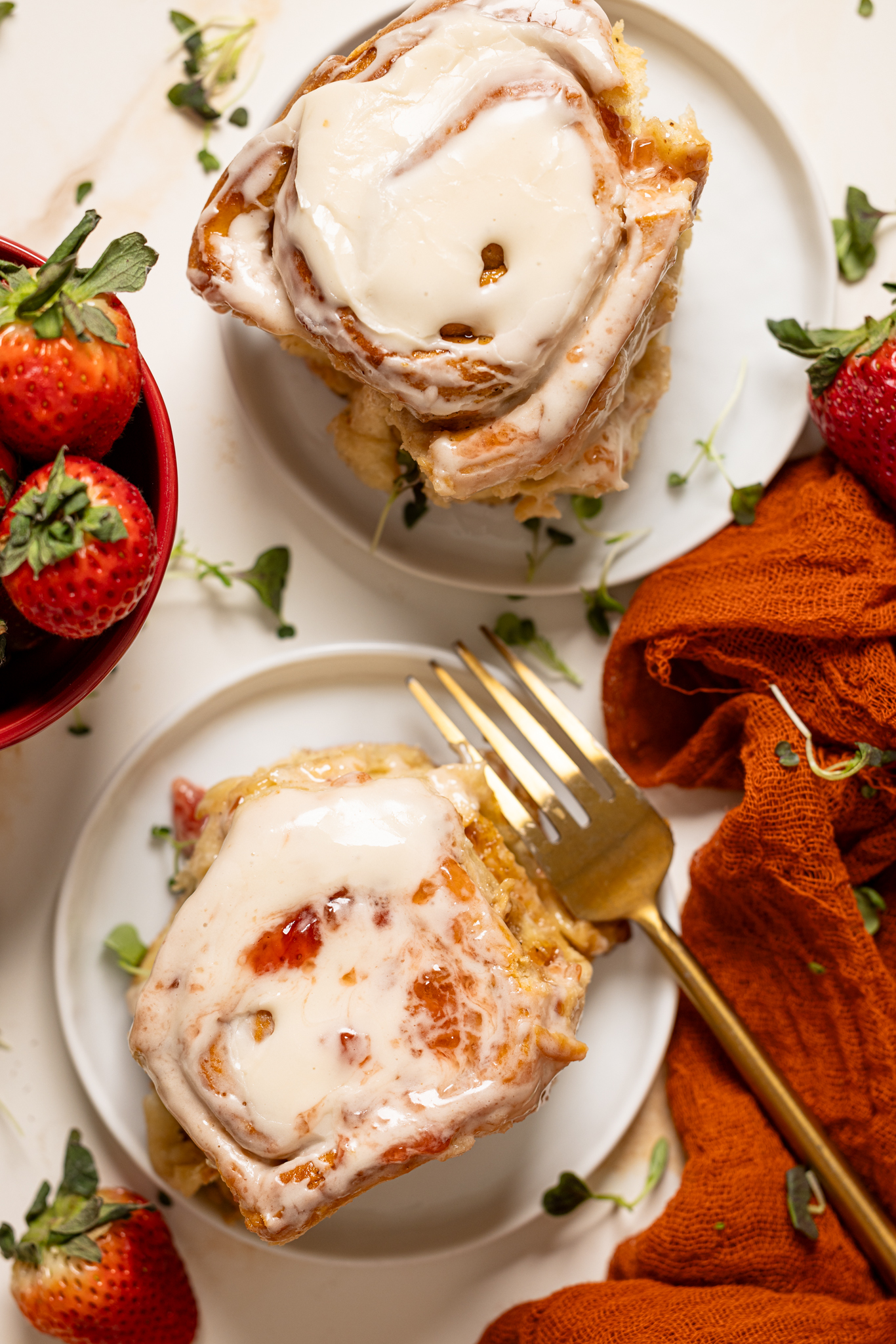 Strawberry shortcake cinnamon rolls on two plates with a fork and strawberries. 